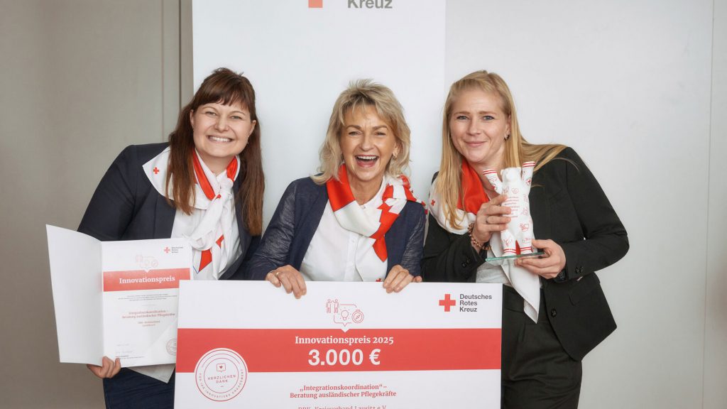 Drei Mitarbeiterinnen des Roten Kreuz halten freudestrahlend einen symbolischen Scheck in die Kamera.