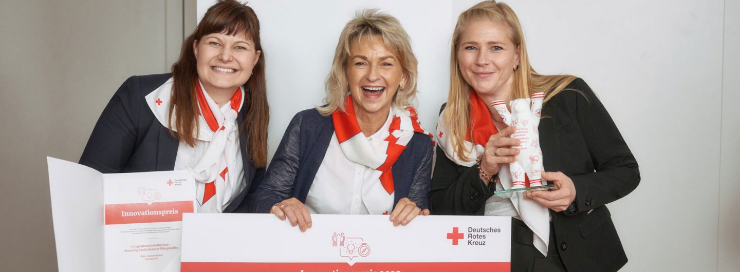 Drei Mitarbeiterinnen des Roten Kreuz halten freudestrahlend einen symbolischen Scheck in die Kamera.