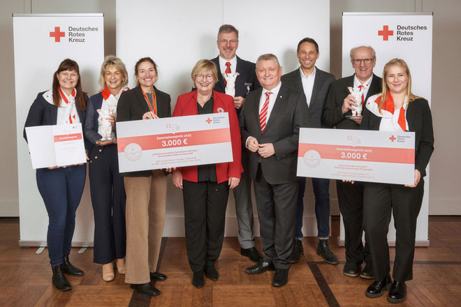 Neun förmlich gekleidete Menschen stehen für ei Gruppenbild vor Rot-Kreuz-Leinwönden und halten symbolische Spendenschecks in den Händen.