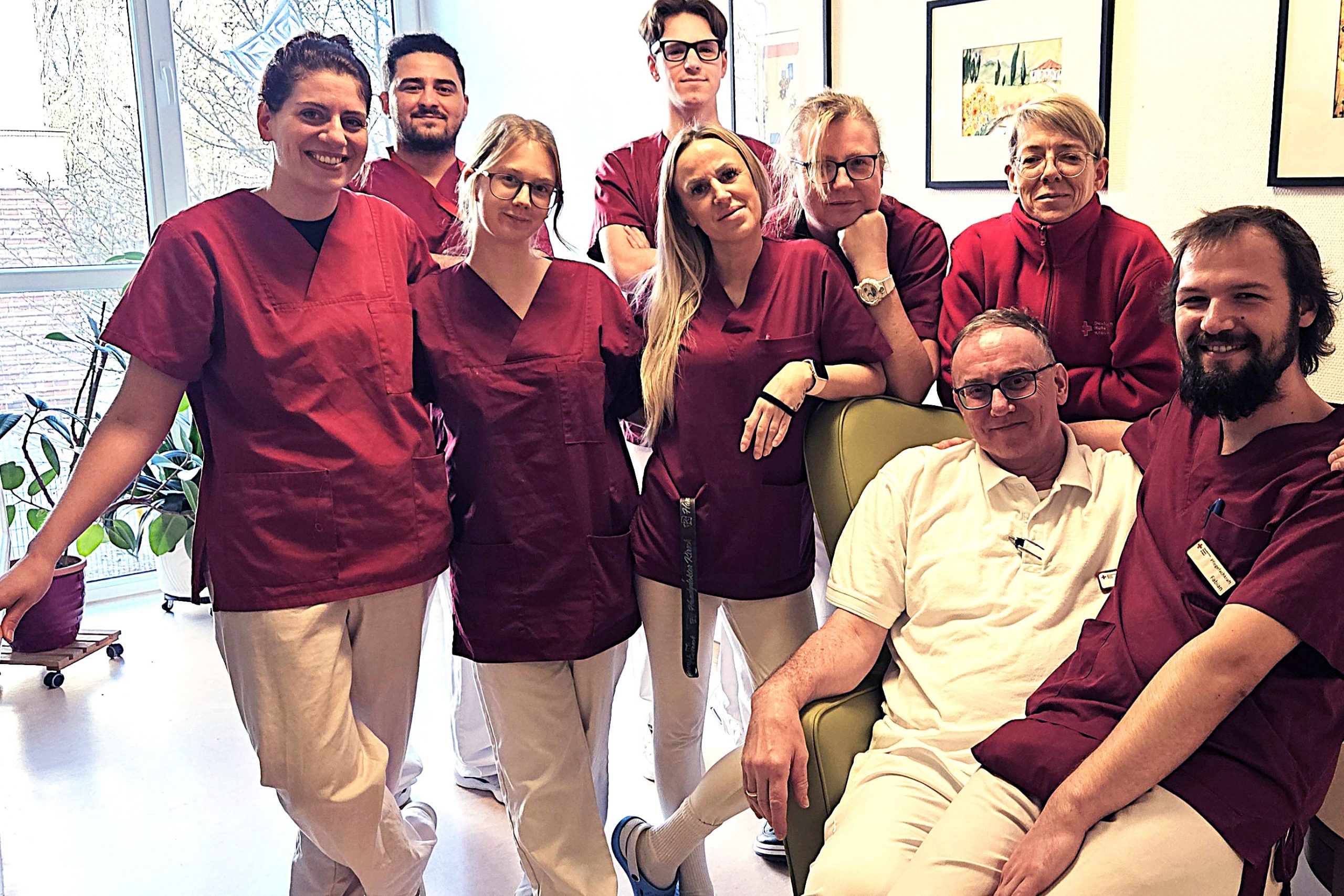 Rund 10 Menschen in Arbeitskleidung einer Pflegeeinrichtung stehen in einer Gruppe zusammen und schauen lächelnd in die Kamera