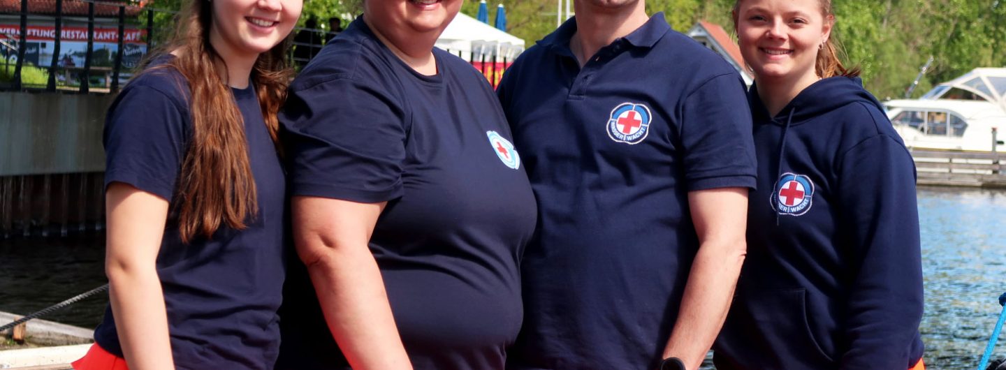 Drei Frauen ud ein Mann stehen in Einsatzkleidung der Wasserwacht des DRK am Wasser.