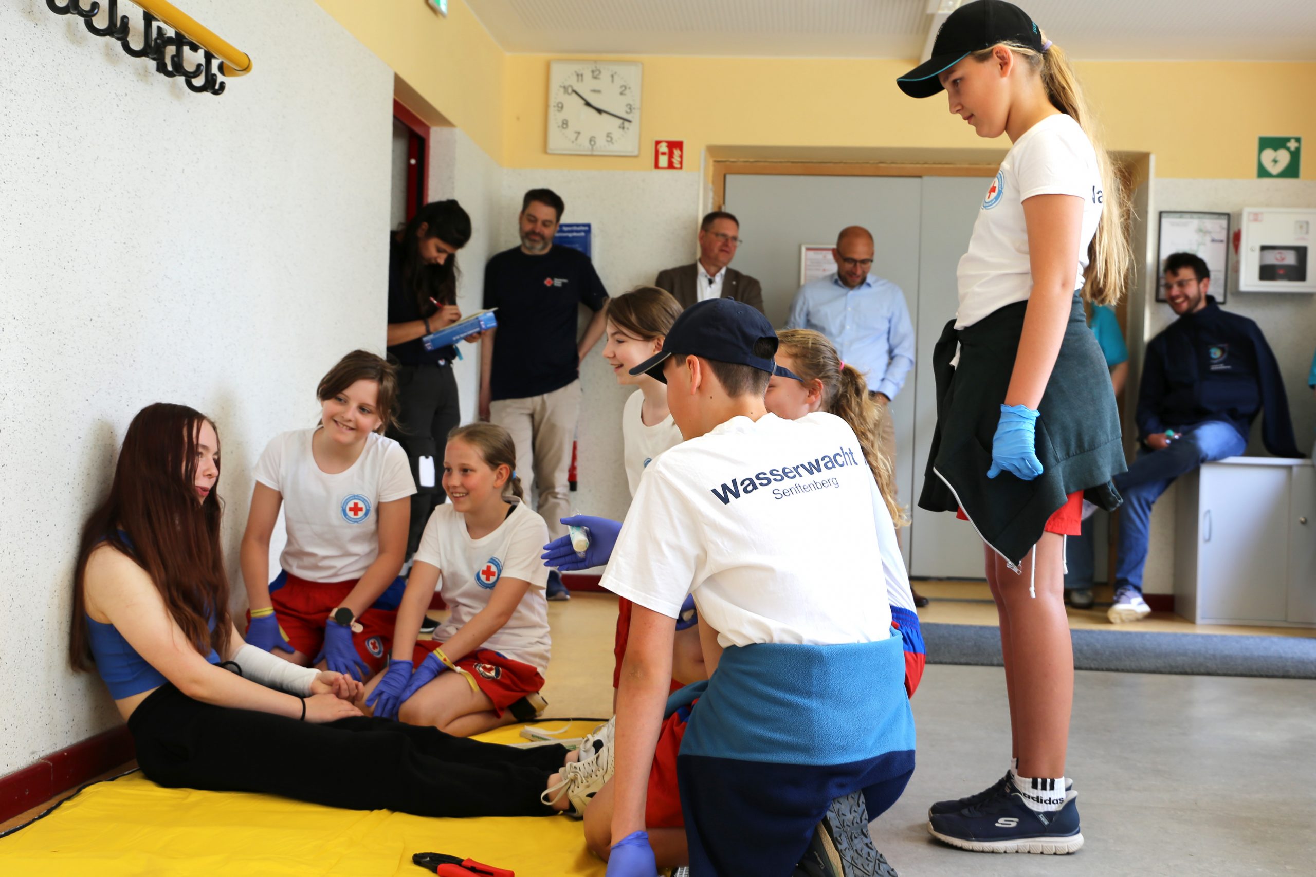 Fünf Kinder in T-Shirts der Wasserwacht des DRK kümmern sich in einer inszenierten Szene um eine Verletzte.