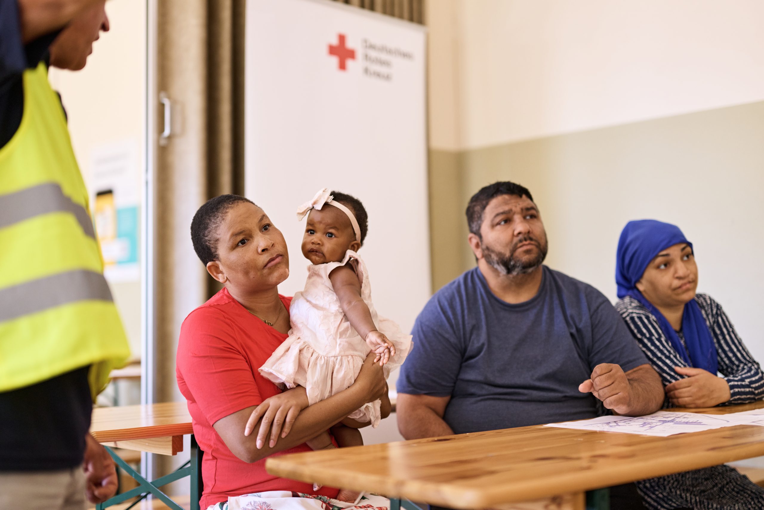 Ein Mann und eine Frau sitzen in einer Unterkunft für Geflüchtete an deinem Tisch. Die Frau hält ein Baby im Arm.